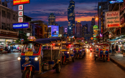 Calle céntrica de Bangkok al anochecer con tuk-tuks y rascacielos iluminados al fondo, ambiente urbano vibrante