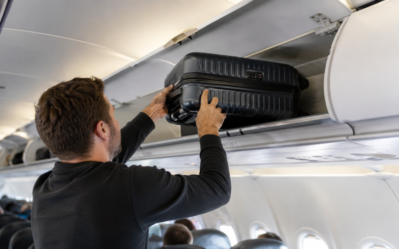 pasajero subiendo una maleta trolley al compartimento superior de un avión