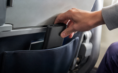 primer plano de una mano guardando un power bank en el bolsillo de un asiento de avión