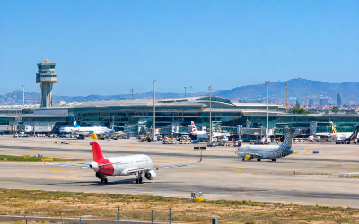 aeropuerto de Barcelona-El Prat con aviones en la pista y terminal al fondo, día soleado de verano